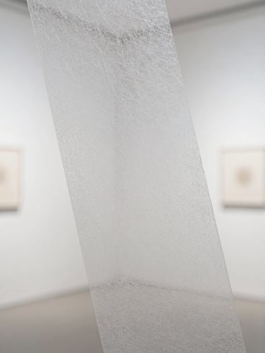 Macro close-up of translucent white fiberglass papercut material, showing the fine fibrous texture, clean cut edges, and subtle light transmission under soft gallery side-light.