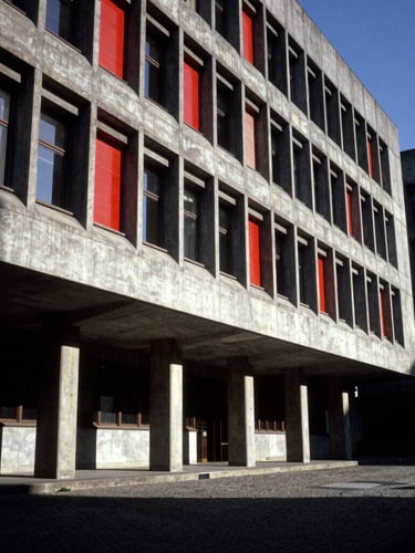 Dramatic wide-angle architectural view of a brutalist concrete government assembly building, high-contrast chiaroscuro lighting, deep shadows and crimson accents, sharp focus, 35mm film grain