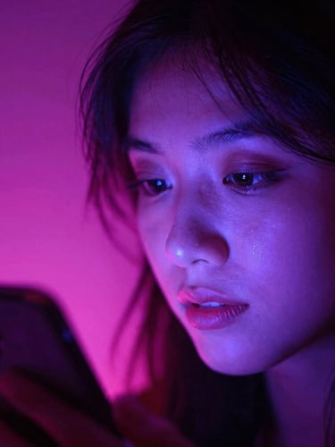 Tight dynamic close-up of a creator's face illuminated by the electric violet glow of a smartphone screen, neon pink backlighting, high contrast, 35mm film grain.