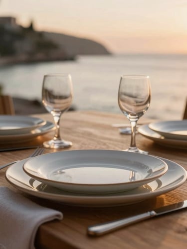 Close-up of a beautifully set dining table with ceramic plates and linen napkins, overlooking a quiet coastal bay at sunset, shallow depth of field