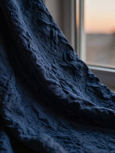 Tactile close-up of organic linen fabric texture, soft twilight window light, deep navy tones, shallow depth of field, 35mm