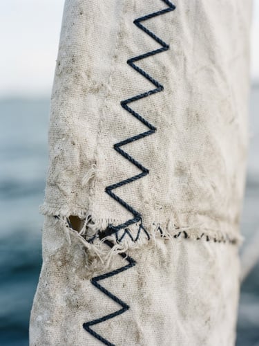 Close-up of weathered white sailcloth texture with heavy zig-zag stitching, soft coastal daylight, minimalist editorial styling, 35mm portrait crop.