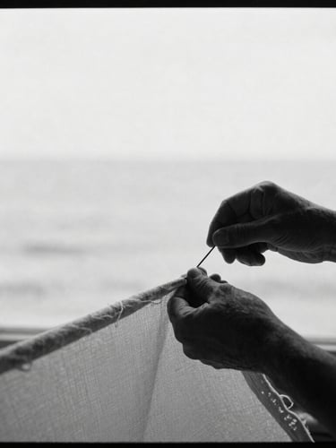 Black and white editorial portrait of an artisan's hands guiding a heavy needle through thick sailcloth under soft window light, authentic, high-contrast, 35mm.