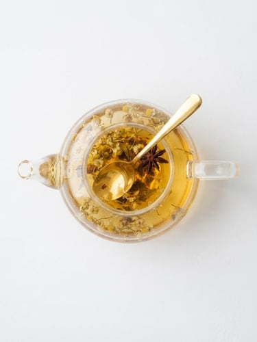 A minimalist overhead shot of an elegant glass teapot filled with golden herbal infusion, soft daylight reflecting off a gold spoon, clean white background