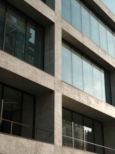 Elegant architectural detail of a modern concrete and glass building, clean straight lines, soft morning light with deep shadows, high-contrast editorial look