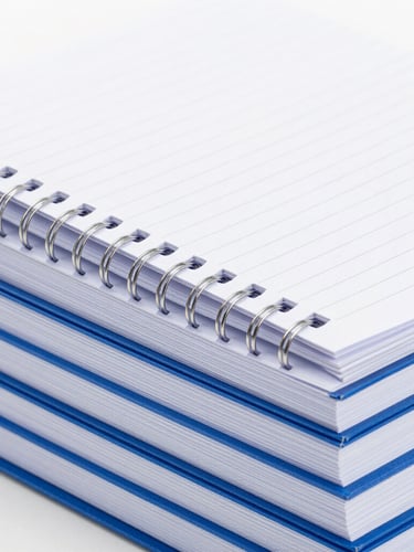 Close-up of durable high-quality notebook thread binding on a stack of blue registers, clean industrial studio lighting, high-contrast white and blue tones