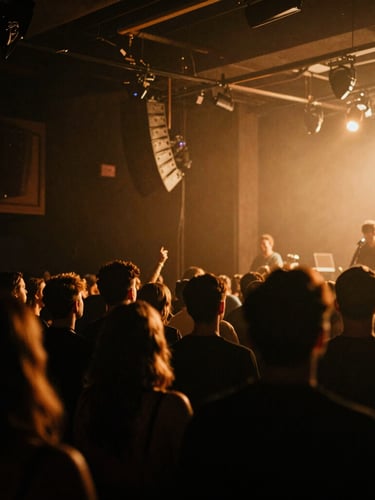 Moody venue interior with low-key concert lighting, dramatic amber backlighting, candid documentary-style shot of a crowd in deep shadow, 35mm film grain.