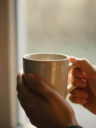 Close-up of hands holding a warm ceramic mug near a window, soft golden-hour light illuminating dust motes, rich organic tones, shallow depth of field, 35mm film aesthetic