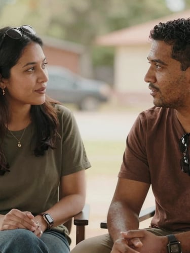 A warm, candid medium shot of two local community leaders in conversation outdoors, soft natural daylight, rich earthy tones, authentic human connection.