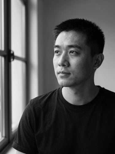 Medium environmental portrait of a designer looking thoughtfully away from the camera, high-contrast natural window light, black and white editorial style