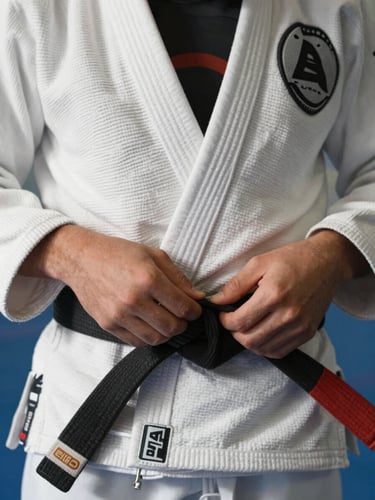 Close-up focado nas mãos de um jovem amarrando a faixa de jiu-jitsu, luz solar natural e brilhante realçando a textura do tecido.
