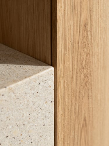 Close-up of natural oak wood meeting raw travertine stone, soft indirect morning light, architectural detail, high texture contrast.