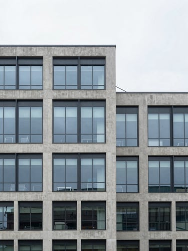 Wide architectural shot of a modern concrete and glass building facade, overcast daylight, muted corporate blues, sharp focus.