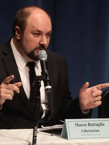 Libertarian candidate Marco Battaglia speaking at a microphone during a political forum event.