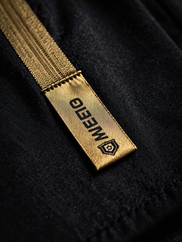 Macro fotografia de um tecido de camisola de futebol oficial, mostrando costuras intrincadas e uma pequena etiqueta de autenticidade, iluminação dramática de estúdio, tons profundos de preto e dourado, 35mm