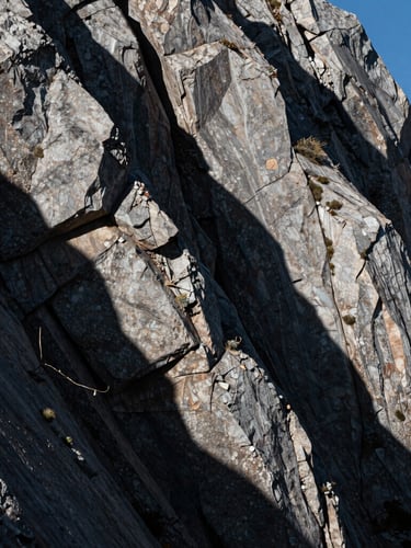 Stark, high-contrast mountain light casting deep shadows on raw stone blocks, architectural composition, portrait orientation.