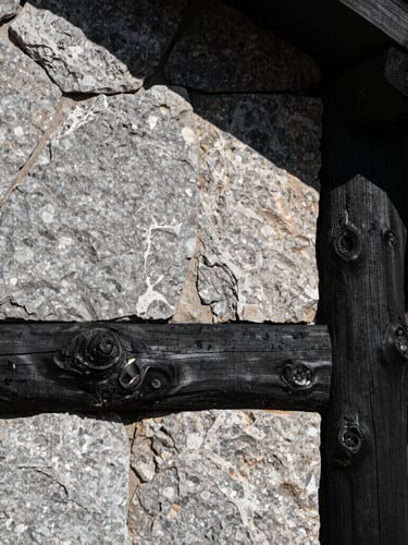 A sharp, high-contrast architectural detail of raw honed stone and charred timber under harsh high-altitude mountain sunlight casting deep shadows