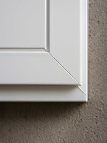 Extreme close-up of a PVC window profile corner weld joint, white surface under diffused north-facing daylight, the mitre line sharp and gap-free, concrete wall texture visible at the frame edge