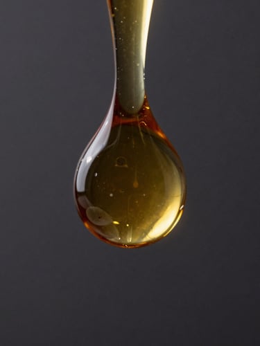 Extreme close-up of a thick amber oil droplet suspending on a glass rod, dark moody background with sharp specular highlights