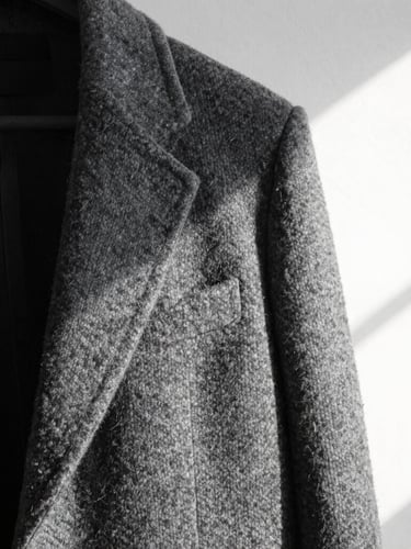 Abstract macro detail of a structured wool coat against a stark white gallery wall, high-contrast directional light, sharp geometric folds.