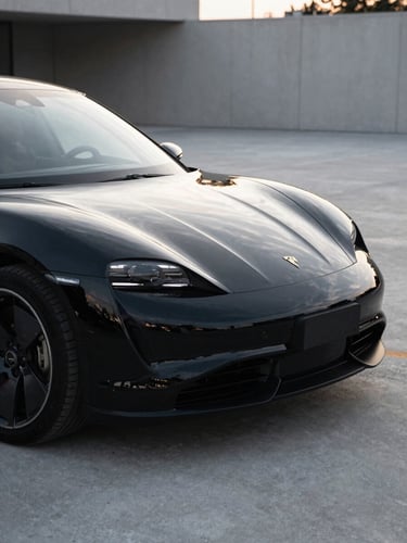 Close-up of a luxury electric car parked in a modern, minimalist concrete driveway in Budapest, soft morning light reflecting off the pristine, freshly detailed black paintwork.