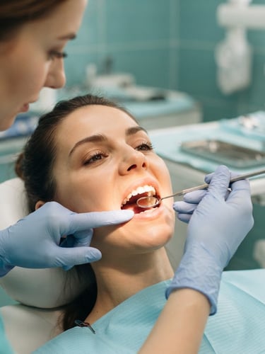 Reassuring close-up of a dentist's gloved hands gently examining a patient's mouth under bright clinical light, sterile equipment in soft focus in background, calming teal tones.