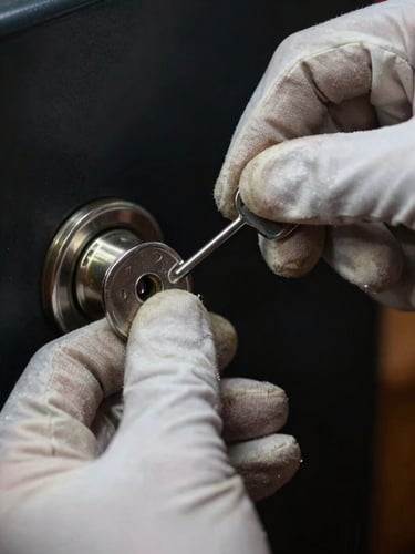 Extreme close-up of a locksmith's gloved hands inserting a pick tool into a residential deadbolt, high-contrast direct strobe lighting, dark background, metal mechanism detail visible, documentary work photography
