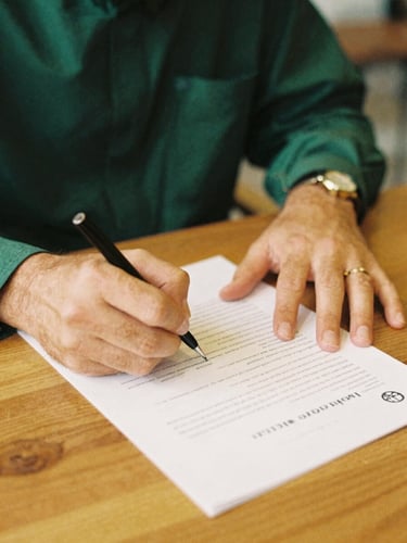 Close up of hands signing a clean Sharia-compliant contract on a warm wooden table, soft golden daylight, rich emerald accents, medium format film
