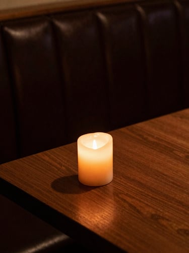 Tight macro crop of a dark leather booth corner, warm amber candle light casting deep shadows on a polished wood table, moody atmosphere.