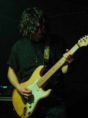 Gritty music photography, high contrast, deep blacks, neon green lights, a musician holding an electric guitar in a dark smoke-filled backstage room, 35mm film grain