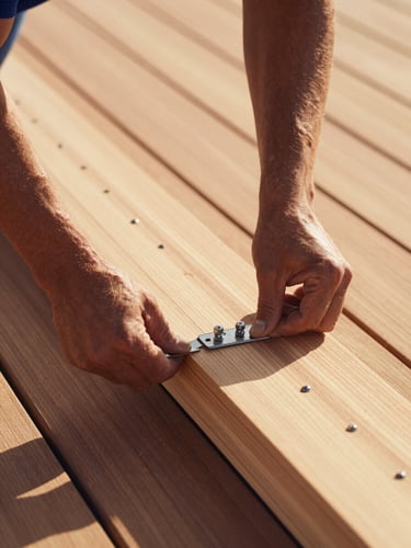 Close-up of a carpenter aligning a premium cedar deck board with hidden fasteners, marine-grade stainless steel hardware visible, bright Pensacola daylight, warm wood tones, shallow depth of field