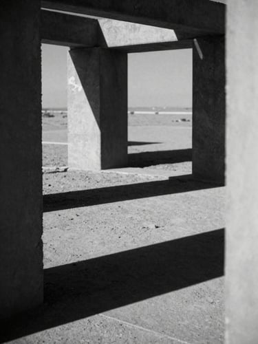 High-contrast black and white photograph of harsh architectural shadows on an abandoned concrete structure in the desert, midday sun, deep ink-black shadows, desaturated tones, 35mm grain