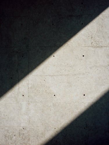 A 35mm film frame of a concrete wall cast in harsh diagonal shadow, high-contrast natural light, desaturated tones