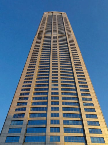 Low-angle heroic shot of a modern Riyadh skyscraper under golden hour sunlight, deep royal blue sky, clean architectural lines, 35mm lens
