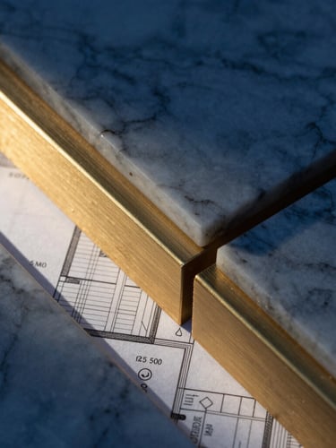 An elegant close-up of premium building materials, marble and brushed gold steel structures, architectural blueprint visible underneath, sharp focus, dramatic lighting