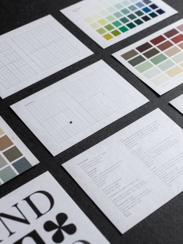 Close-up overhead flat-lay of a structured brand identity system laid out on a dark matte surface — printed brand guidelines, geometric grid overlays, colour swatch cards, and typographic specimen sheets arranged with architectural precision, cool studio lighting, high contrast, no people, documented not performed