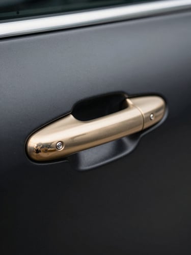 Close-up of a luxury car door handle in polished champagne gold against a matte black door panel, cool studio light catching the metal edge with precision, shallow depth of field, no background distraction — the detail reads as a tactile credential