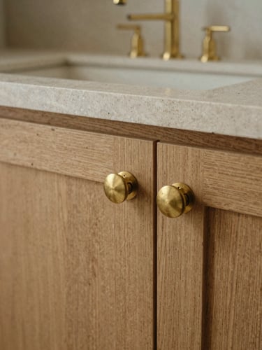 A close-up of raw honed limestone and brushed brass hardware on grain-matched oak, natural side-lighting, medium format film.