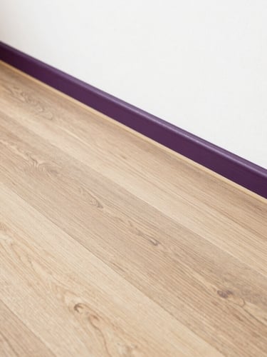 Detail shot of perfectly aligned laminate wood flooring meeting a clean white wall, warm natural light, architectural precision