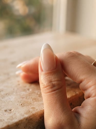 Macro editorial photograph of sculpted nail architecture, soft golden-hour window light, rich travertine background, shallow depth of field, 35mm