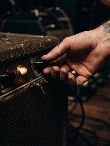 Close-up of weathered hands adjusting the volume knob of a vintage tube amplifier, warm tungsten pilot light glowing amber in a dark room, 35mm film grain
