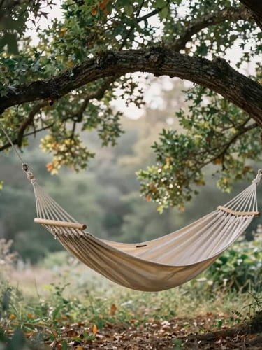 Soft editorial photography of a canvas hammock suspended high in a massive green oak tree, filtered golden forest light, shallow depth of field, 35mm