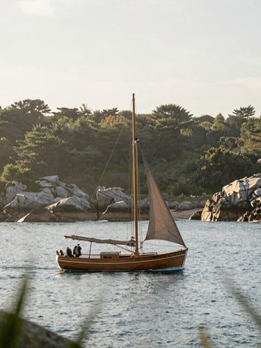 Soft editorial photography of a classic wooden sailboat gliding on calm blue Atlantic waters near the rocky Breton coast, soft overcast daylight, poetic atmospheric framing
