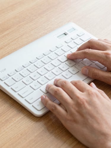 Close-up of hands using an adaptive keyboard and braille display on a wooden desk, clean high-contrast daylight, sharp focus.