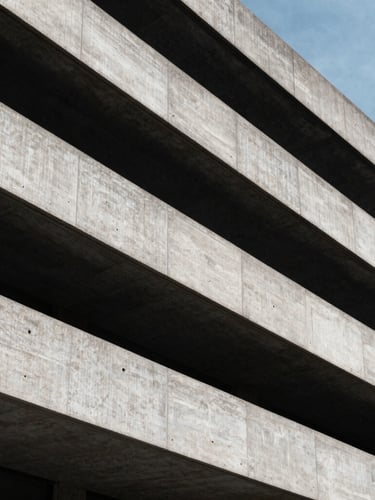 Low-angle heroic shot of brutalist London concrete architecture, hard directional daylight, deep shadows, cool gray tones, 35mm lens