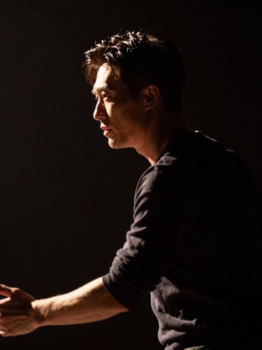 Dramatic low-key stage lighting from the side, highlighting the intense profile of an actor in motion, dark background, cinematic 16:9 framing.