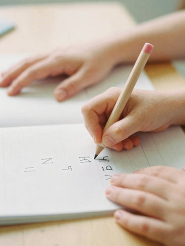 Close-up of a child's hand and a parent's hand gently guiding a crayon over a printed letter on a workbook, soft morning light, on a wooden table, warm editorial photography, 35mm film look