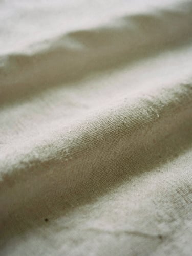 Macro film photography of soft textured cotton fabric, warm overcast daylight, muted oat tones, shallow depth of field, 35mm.