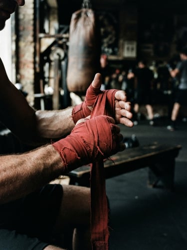 Close-up of an athlete's hands wrapping in red cotton wraps, high-contrast side lighting with dramatic shadows, gritty gym texture, 35mm film