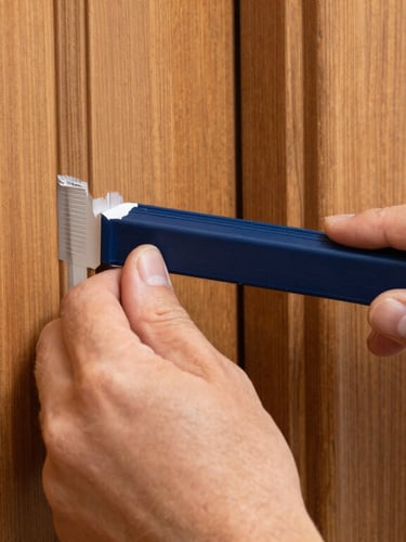 Bright architectural detail shot of a professional painter tape line, crisp paint edge against a warm wood door frame, clean hands, natural light, macro photography